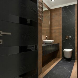 Sleek bathroom with black marble tiles and wooden accents, featuring a modern sink and toilet.