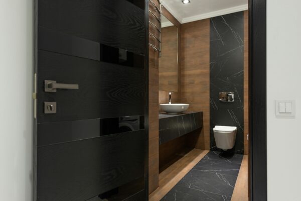Sleek bathroom with black marble tiles and wooden accents, featuring a modern sink and toilet.